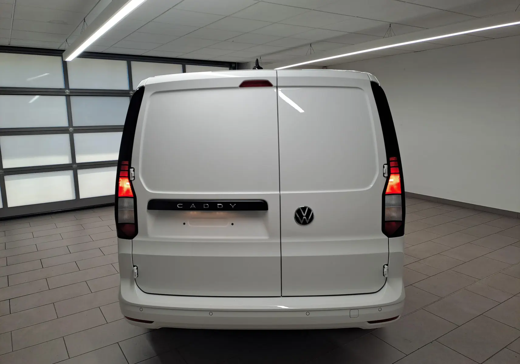 Vue arrière du Volkswagen Caddy Cargo Maxi blanc Candy 2026 avec feux allumés et logo VW visible.
