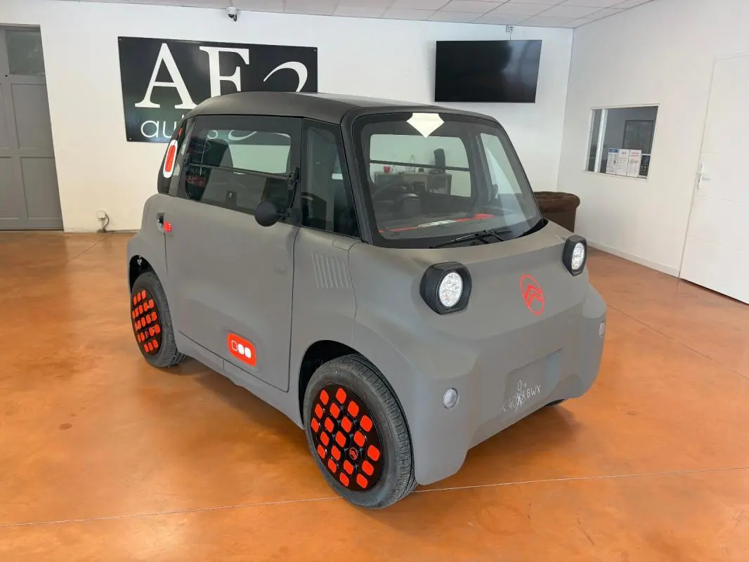 Vue 3/4 avant droite d'une Citroën AMI Spicy grise électrique 2025 avec jantes et logos orange distinctifs.