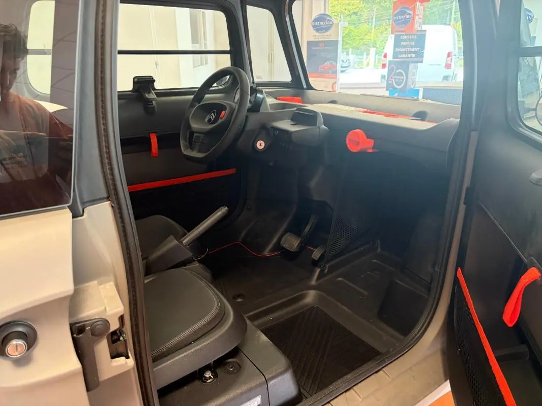 Intérieur de la Citroën AMI Spicy 2025 gris, vue côté conducteur, avec détails orange vif sur tableau de bord et portes.