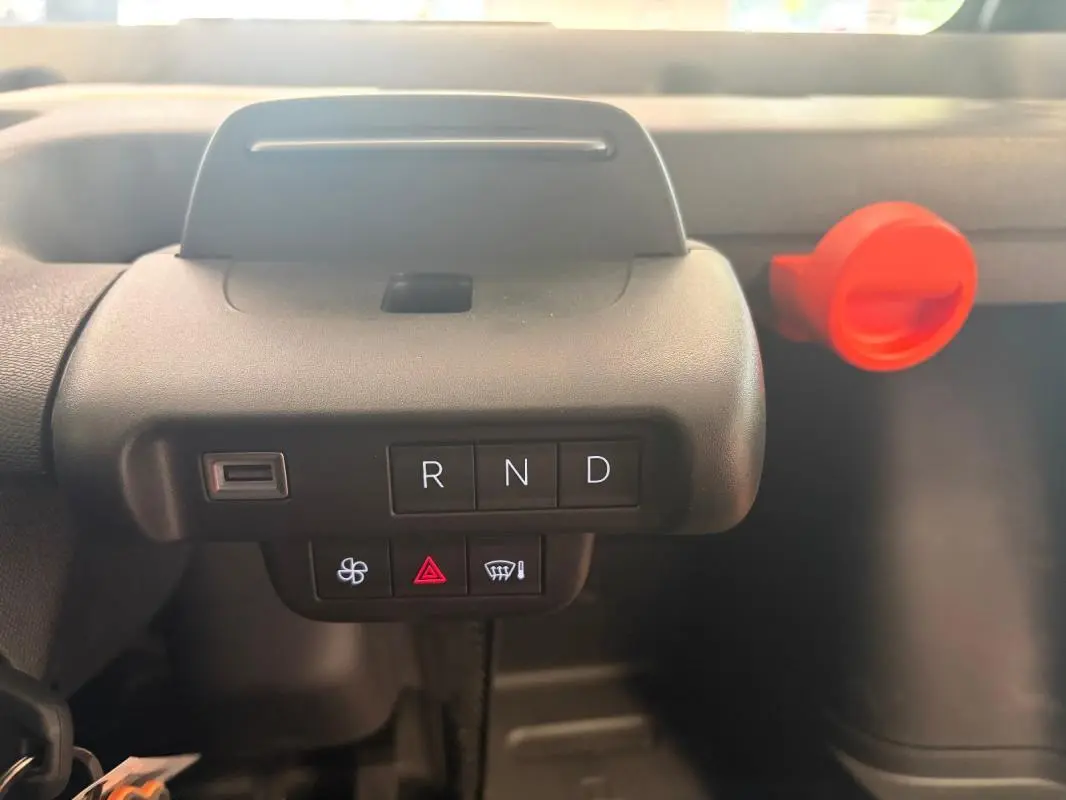 Gros plan sur la console centrale de la Citroën Ami Spicy 2025 grise, montrant les boutons de boîte auto R, N, D et un bouton rouge d'alerte.
