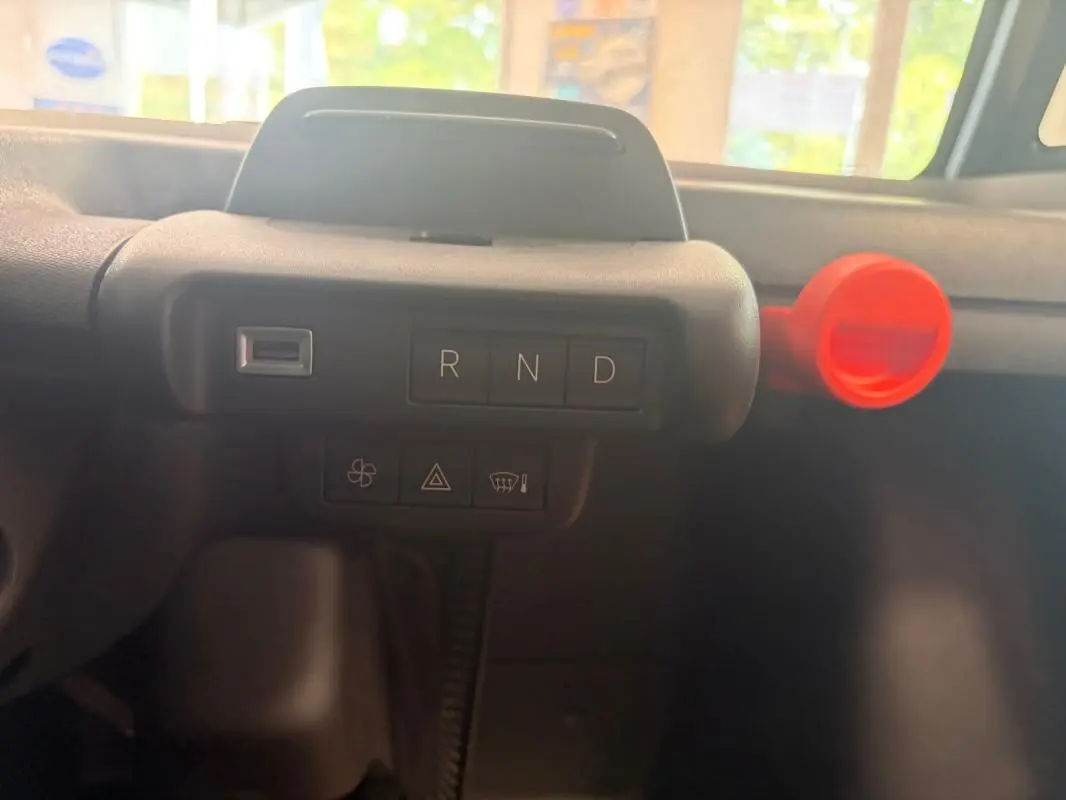 Détail du tableau de bord de la Citroën Ami Spicy 2025, montrant la commande de boîte auto gris foncé avec bouton rouge.
