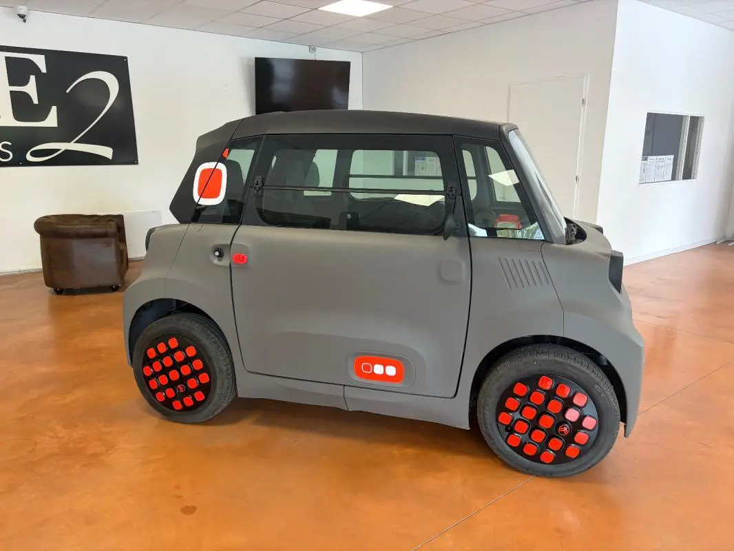 Vue de profil droit de la Citroën Ami Spicy gris 2025 avec détails rouges distinctifs sur les roues et la carrosserie.