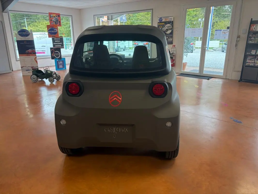 Vue arrière du Citroën Ami Spicy gris 2025, compacte et électrique, avec feux ronds rouges et logo Citroën éclairé.