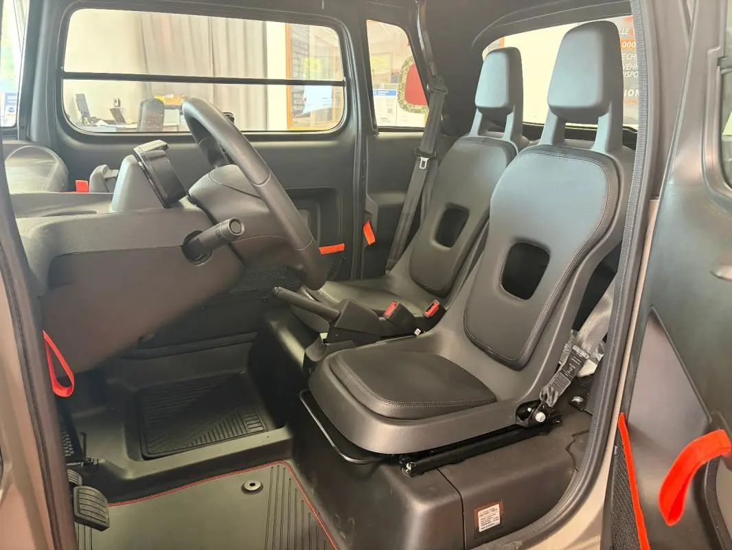 Vue intérieure côté gauche du Citroën Ami Spicy 2025 gris, montrant les sièges noirs et détails orange vifs.