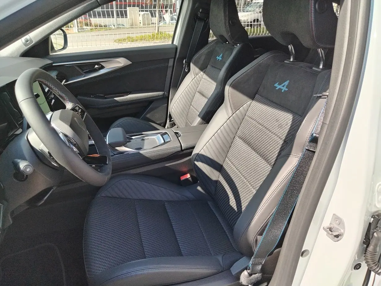 Vue intérieure côté conducteur du Renault Austral E-Tech blanc nacré, sièges sport noirs avec logo Alpine bleu brodé.