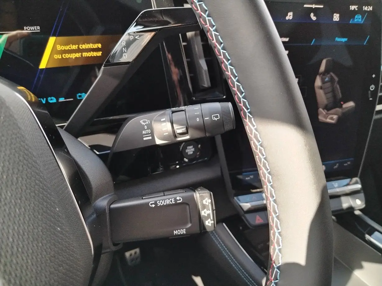 Gros plan sur le volant avec surpiqûres tricolores et commandes, tableau de bord numérique du Renault Austral E-Tech 2025.