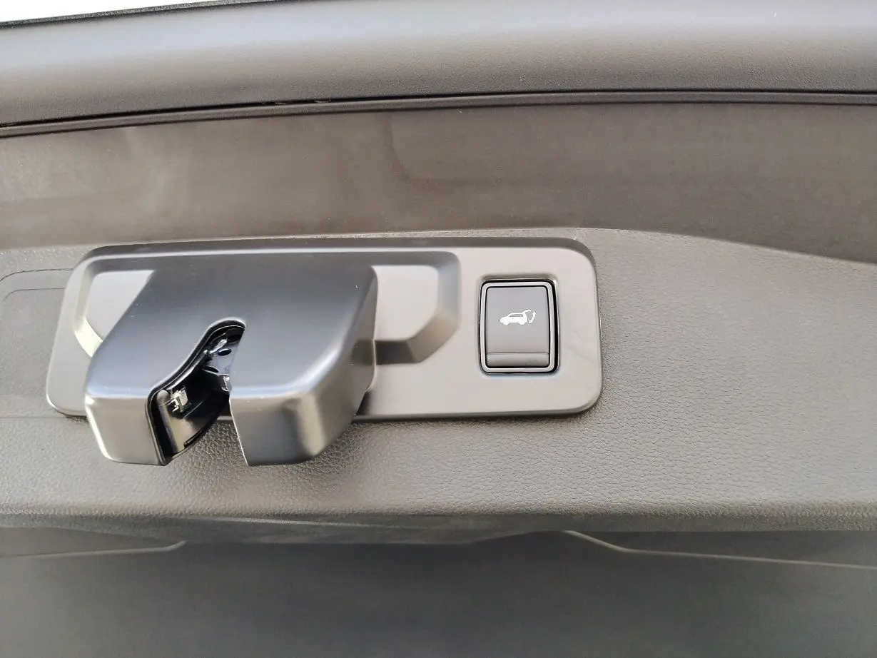 Gros plan sur la poignée de coffre avec bouton d'ouverture électrique du Renault Austral blanc nacré toit noir.