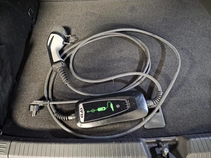 Câble de recharge noir pour Volkswagen Golf hybride rechargeable posé dans le coffre au revêtement gris.