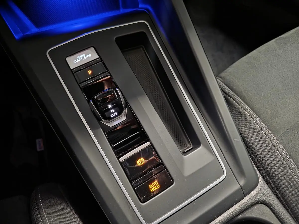 Vue rapprochée de la console centrale de la Volkswagen Golf gris, montrant la commande de boîte auto DSG et le frein à main électronique.