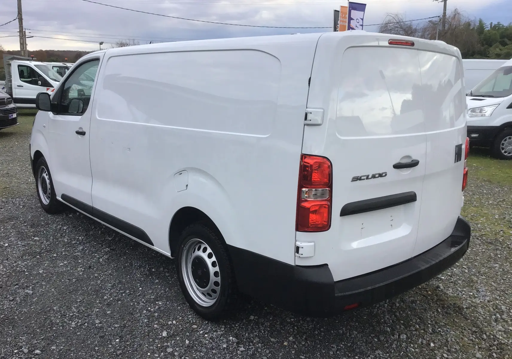 Fiat Scudo Fourgon blanc en vue 3/4 arrière droit, fourgon utilitaire avec garde au sol réhaussée et plaque de protection.