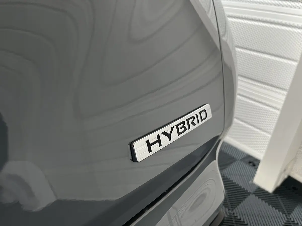 Gros plan sur l’inscription Hybrid sur la portière côté droit d’un Nissan Juke gris clair 2024.