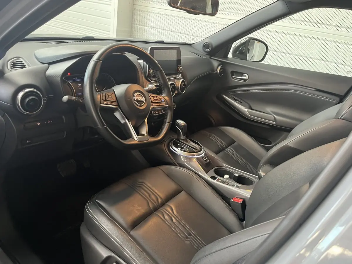 Vue intérieure côté conducteur du Nissan Juke Hybrid 2024, sièges cuir noirs et tableau de bord avec écran tactile central.