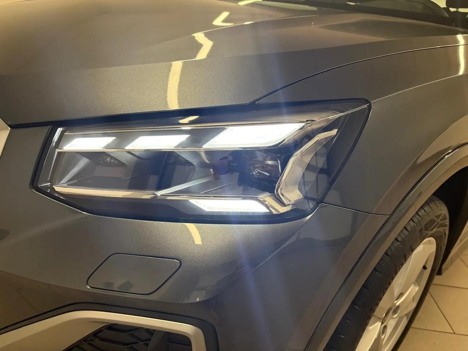 Gros plan sur le phare avant droit allumé d’un Audi Q2 35 TFSI S Line gris Daytona avec peinture métallisée.