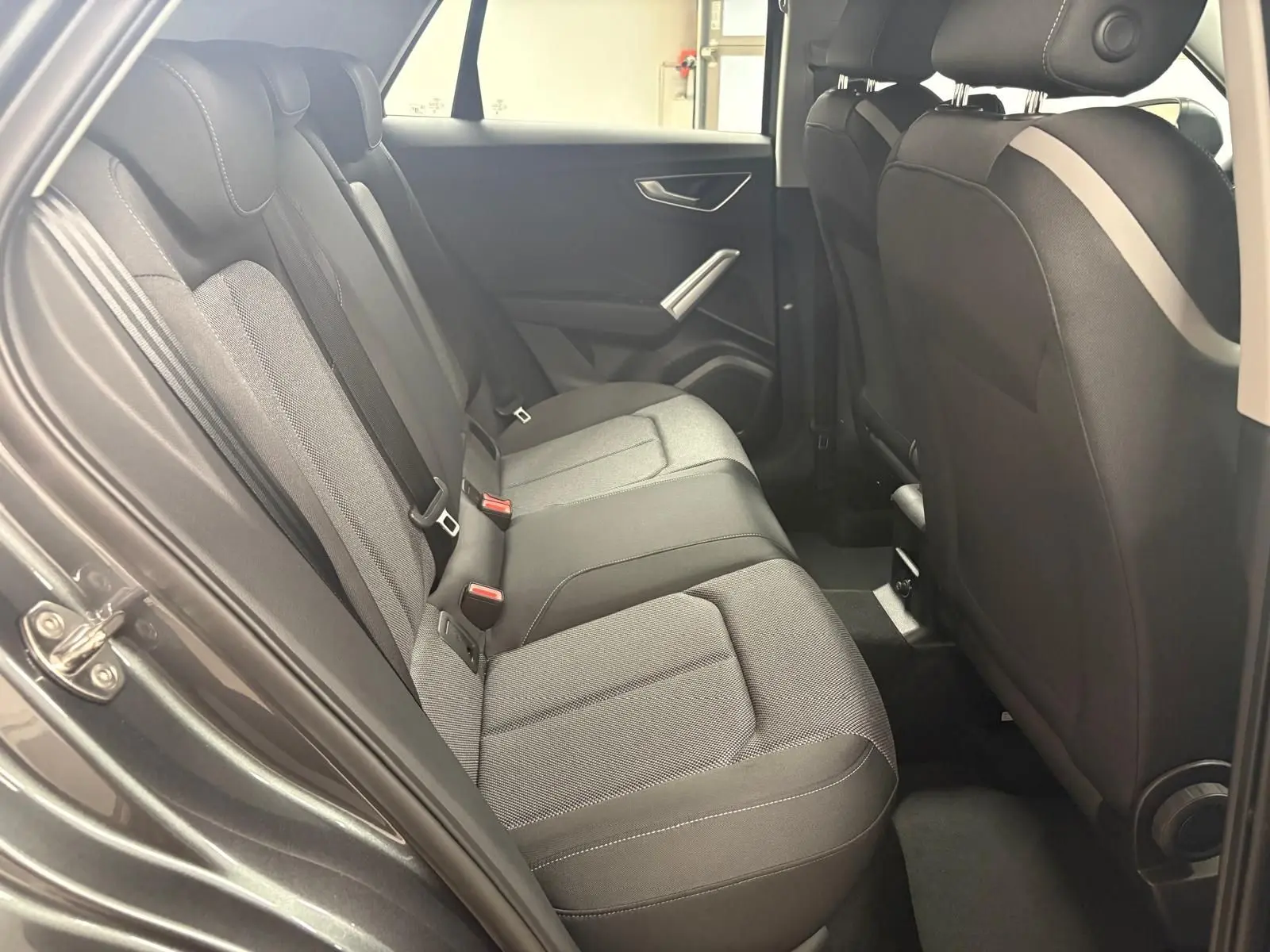 Vue intérieure de la banquette arrière de l'Audi Q2 35 TFSI S Line 2026 avec sellerie tissu gris et portes ouvertes côté gauche.