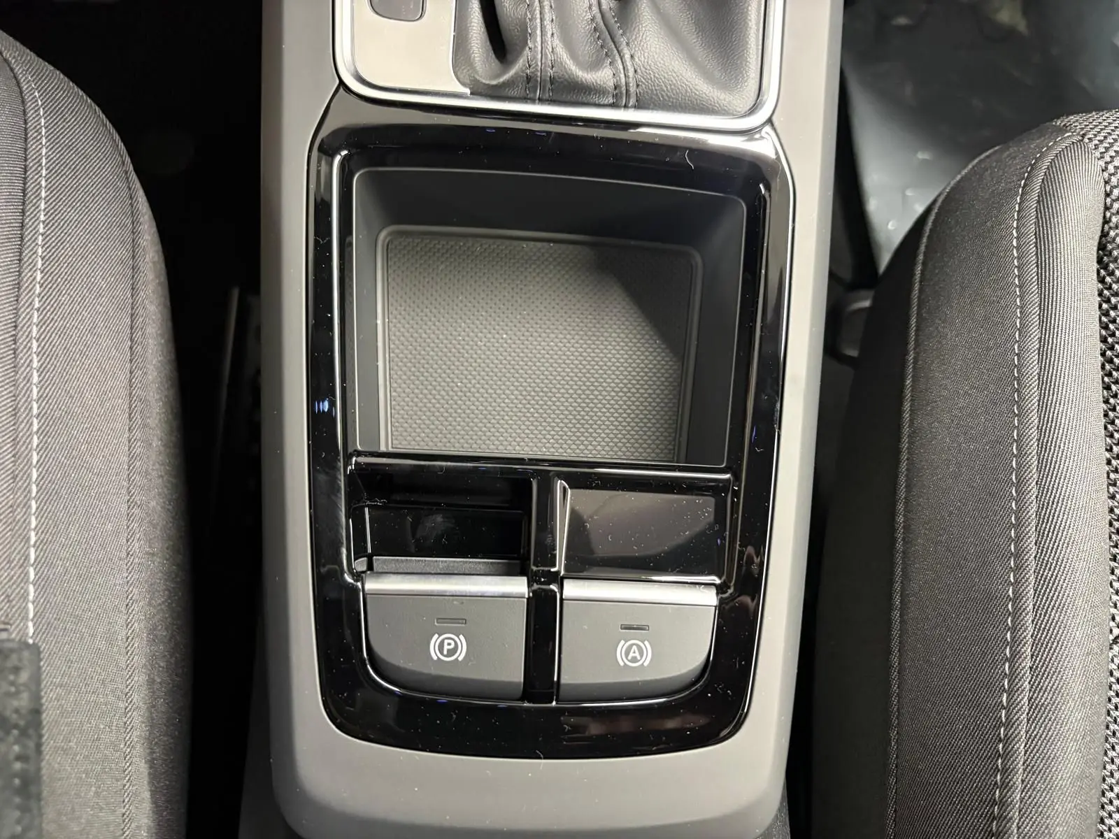 Gros plan sur la console centrale noire brillante entre les sièges avant en tissu gris de l'Audi Q2 35 TFSI S Line.