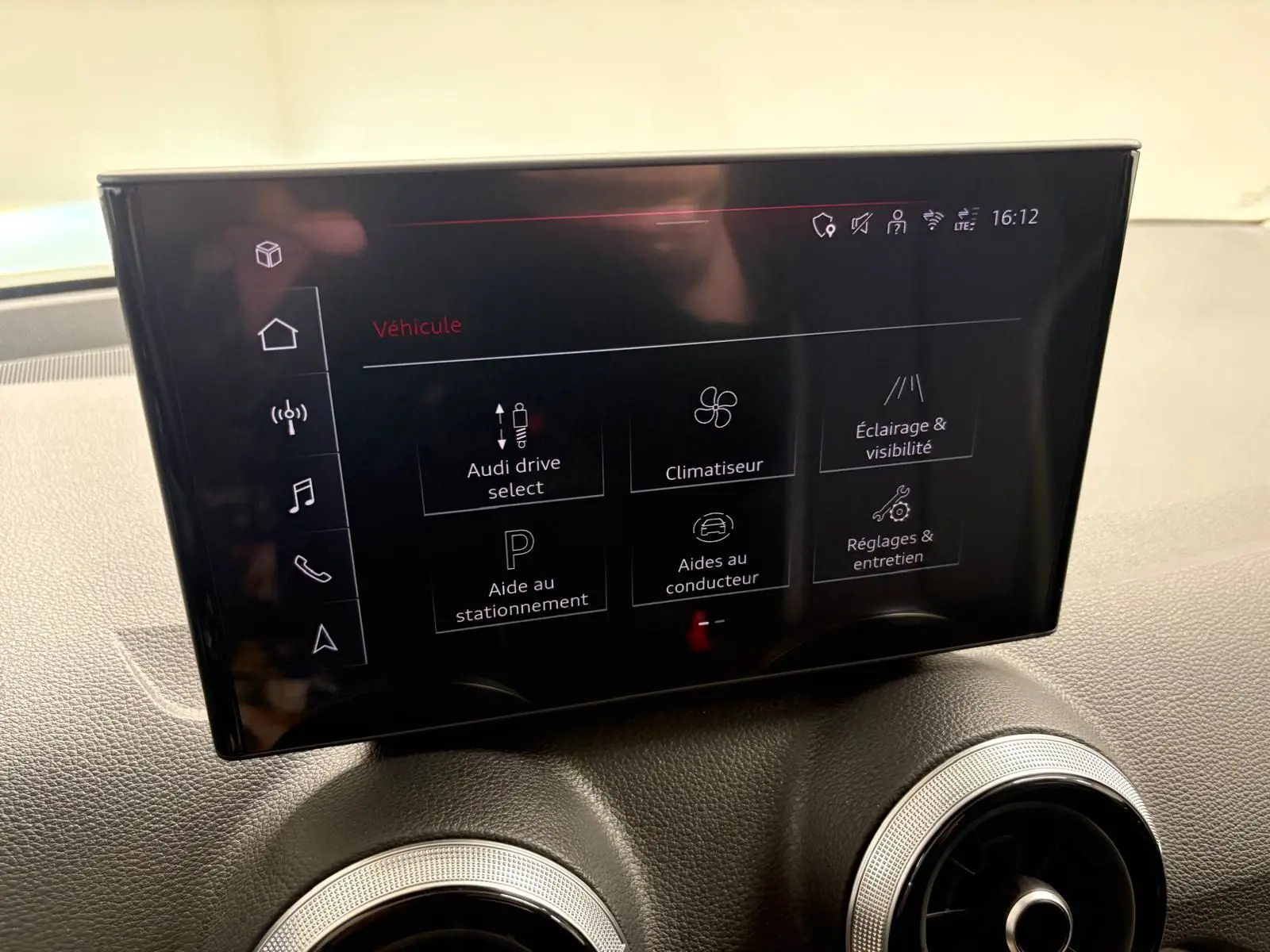 Écran tactile central de l’Audi Q2 35 TFSI S Line 2026, affichant les réglages du véhicule, avec tableau de bord gris.