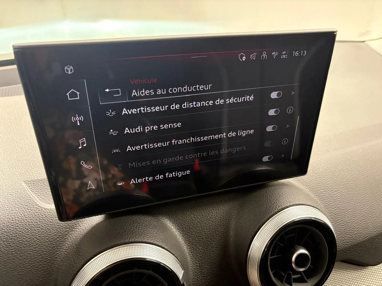 Écran central intérieur de l'Audi Q2 35 TFSI 150 S Line 2026 affichant les aides à la conduite, avec aérateurs ronds en dessous.
