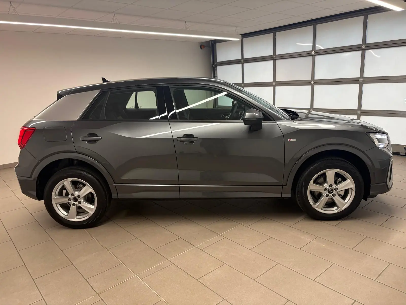 Audi Q2 35 TFSI S Line gris Daytona vue de profil côté gauche dans un garage, avec jantes alliage visibles.