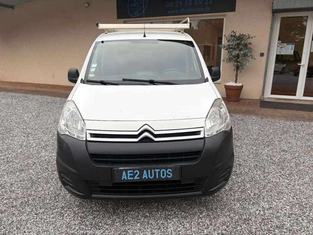 Vue de face d’un Citroën Berlingo blanc 2018 avec pare-chocs noir et galerie de toit, stationné sur gravier.