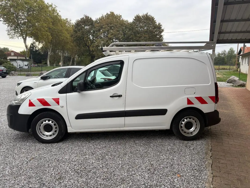 Vue de profil côté gauche d’un Citroën Berlingo blanc fourgon 2018 avec bandes rouges réfléchissantes et galerie sur le toit.