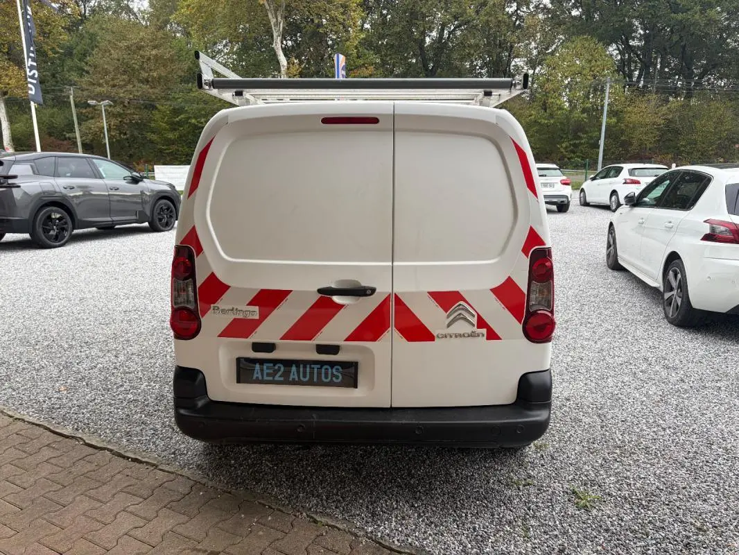 Vue arrière d’un Citroën Berlingo blanc 2018 avec bandes rouges réfléchissantes et porte-échelle sur le toit.