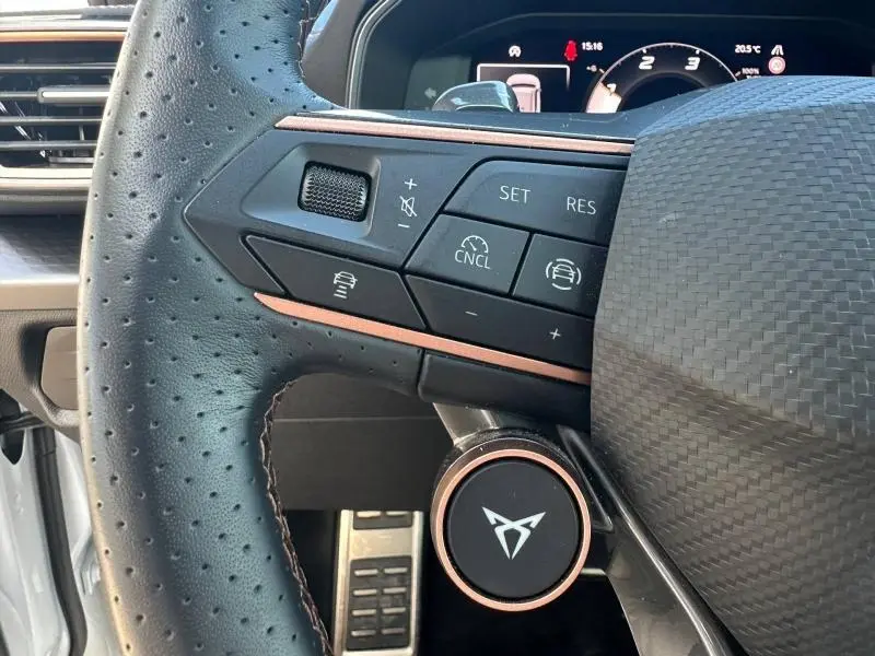 Gros plan sur le volant perforé du CUPRA Formentor blanc Nevada, avec commandes multifonctions et logo CUPRA en relief cuivre.