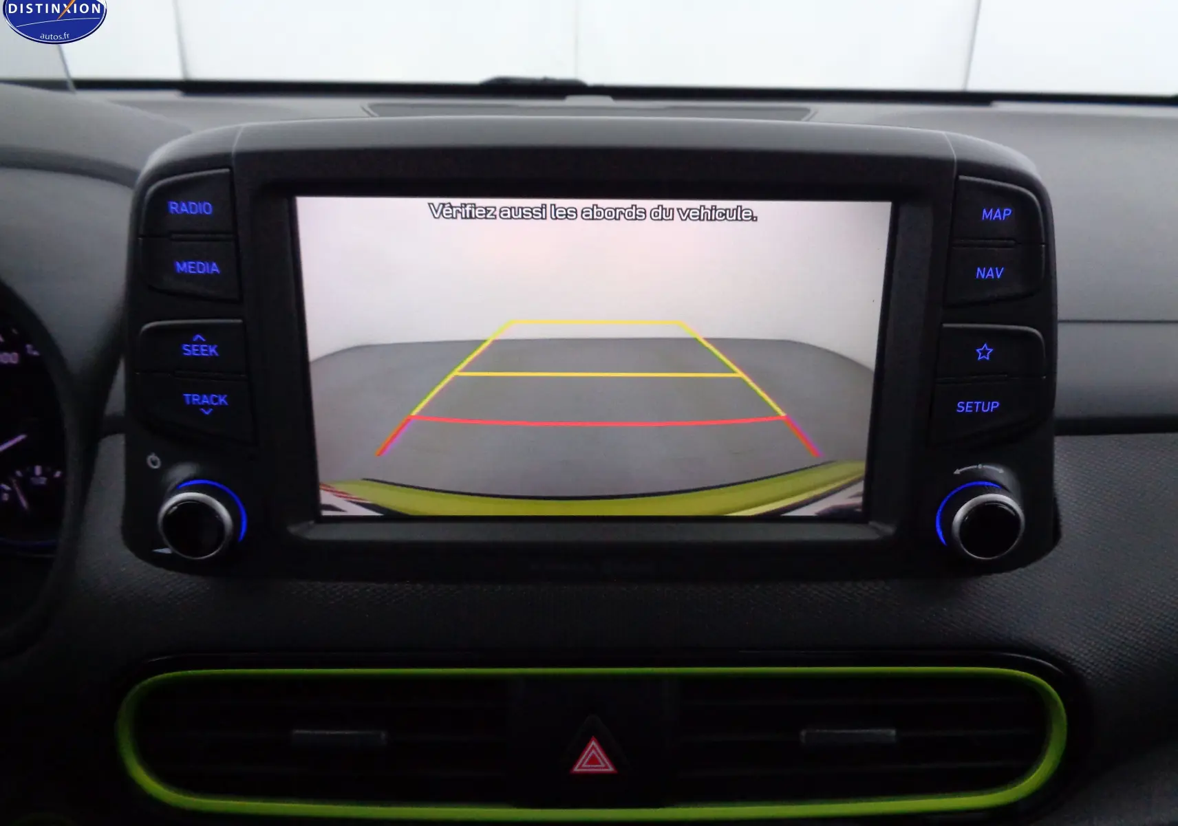 Écran de caméra de recul affichant l'arrière du Hyundai Kona jaune acidulé, avec commandes multimédia autour.