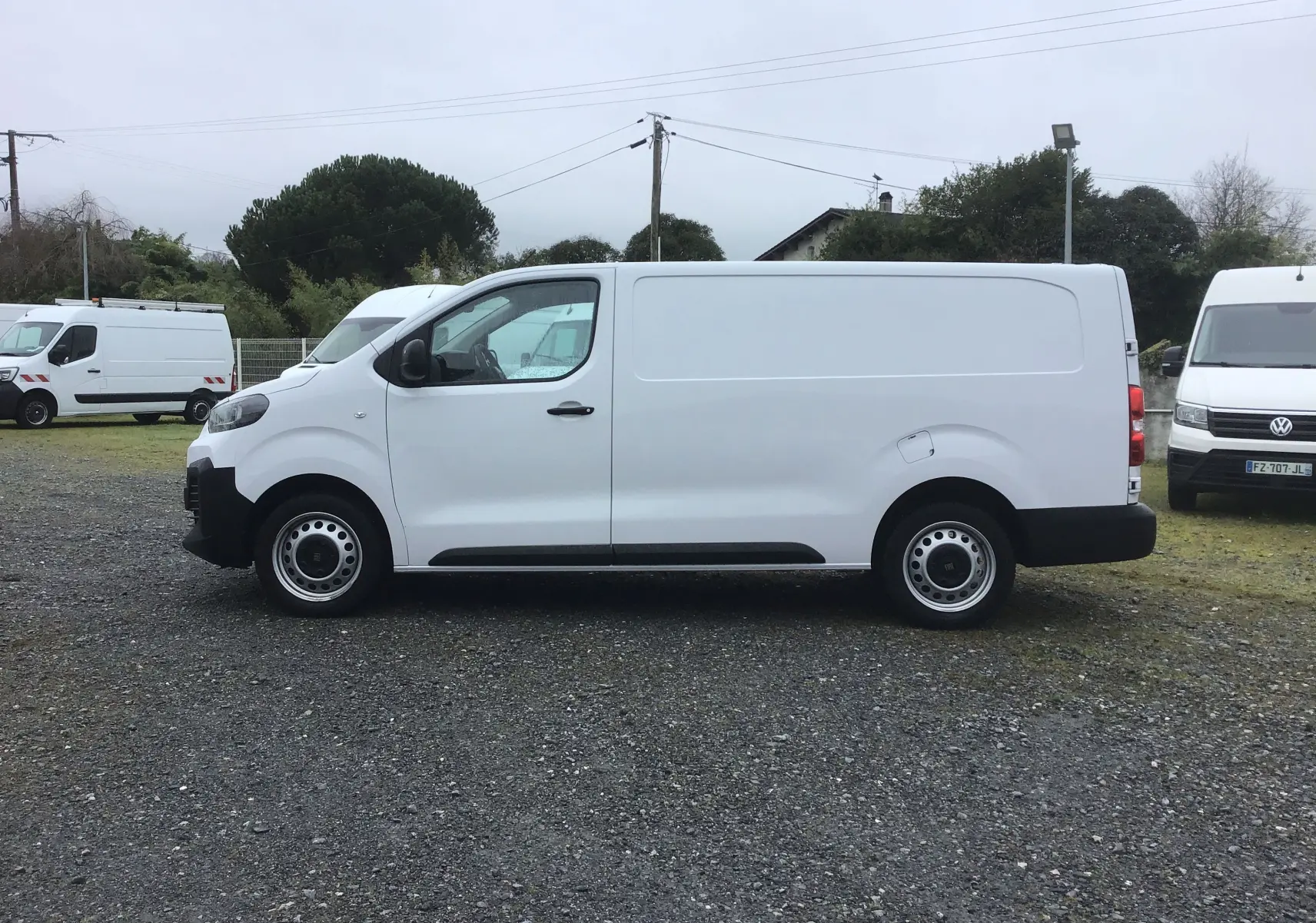 Vue de profil côté gauche d’un FIAT Scudo Fourgon blanc 2024 avec garde au sol réhaussée et protections noires visibles.