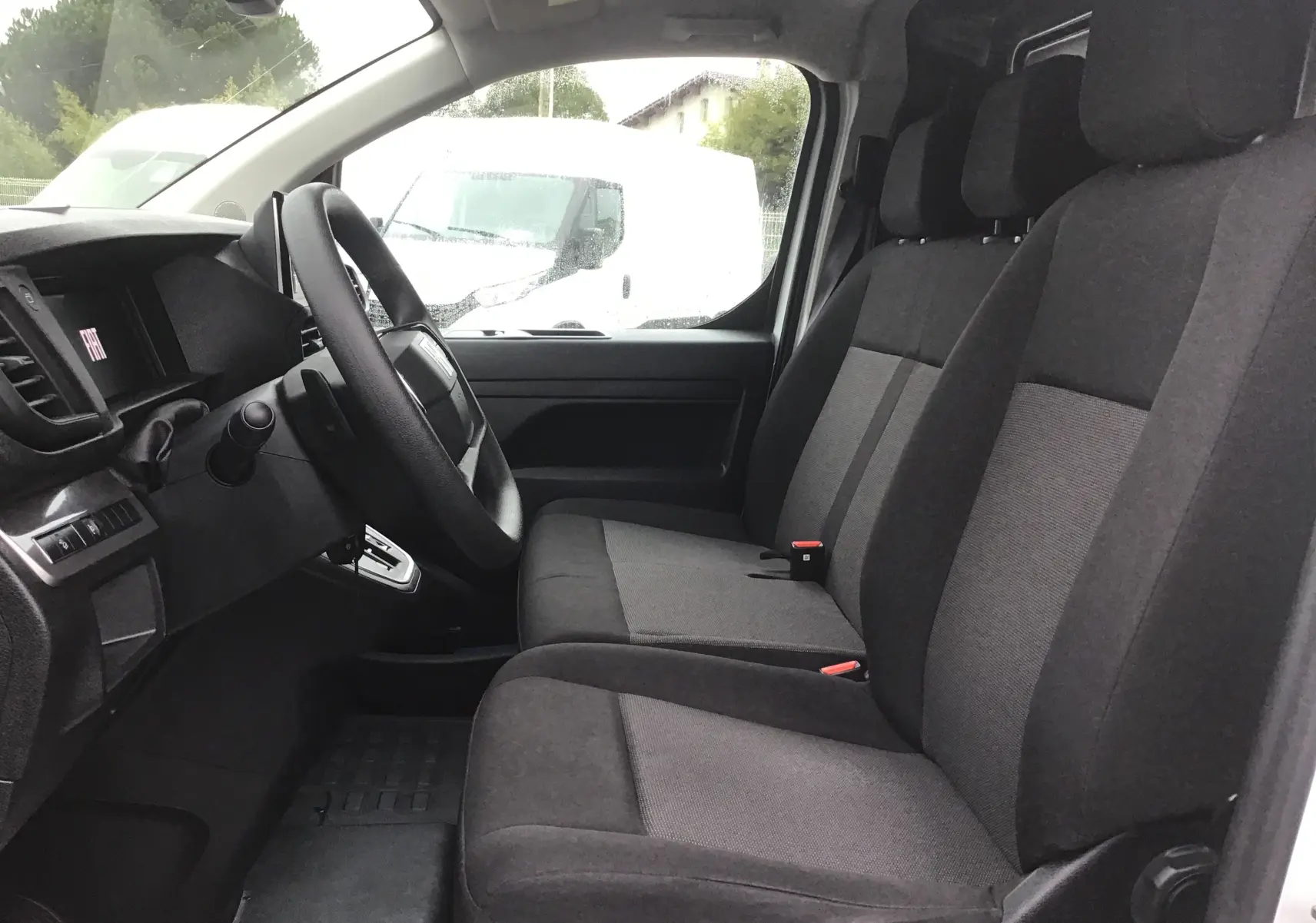 Vue intérieure côté conducteur du Fiat Scudo Fourgon blanc 2024, montrant les sièges avant en tissu gris et le tableau de bord.
