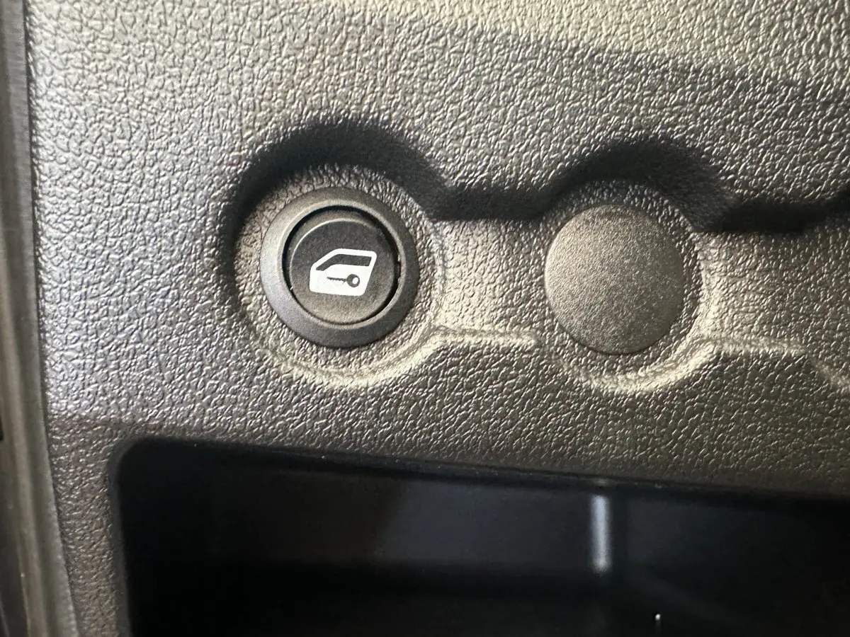 Gros plan sur un bouton de commande de coffre dans l’habitacle noir texturé de l’AIXAM AMBITION 0.5 CITY GTO blanc.