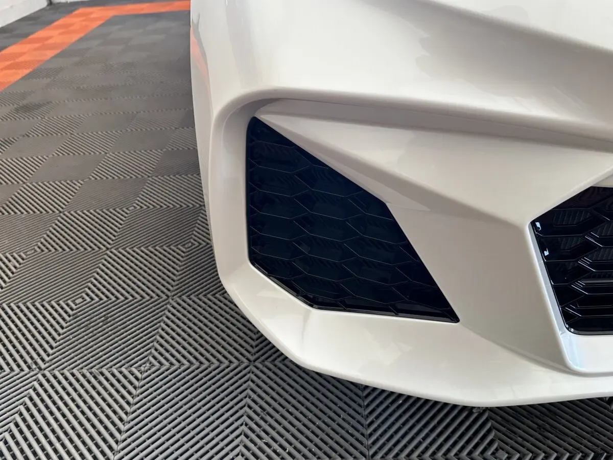 Gros plan sur l'entrée d'air avant gauche d'une Aixam Ambition 0.5 City GTO blanche, soulignant sa calandre noire hexagonale.