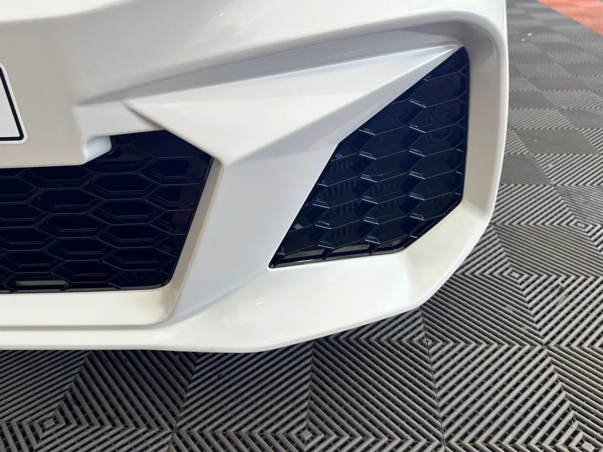 Gros plan sur la partie avant droite blanche de l'AIXAM AMBITION 0.5 CITY GTO avec grille noire hexagonale.