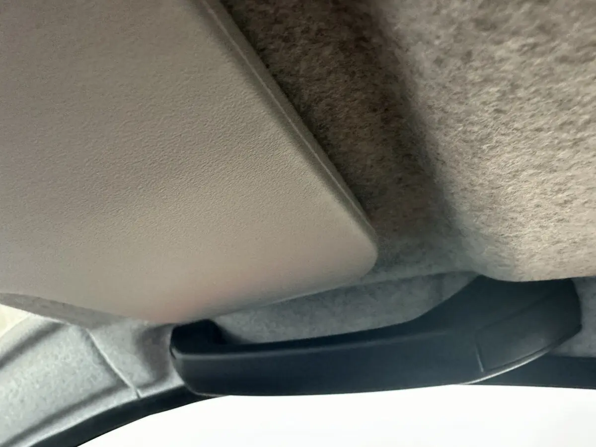 Poignée de maintien noire fixée au plafond intérieur d'un véhicule, avec revêtement gris clair en tissu.
