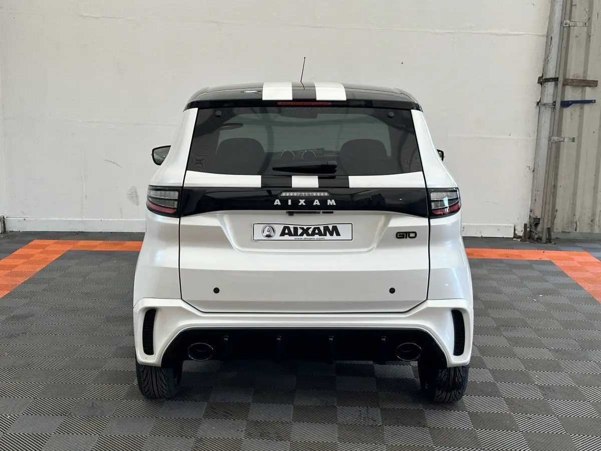 Vue arrière d'une Aixam Ambition 0.5 City GTO blanche avec toit noir et bandes noires, en intérieur sur sol carrelé.