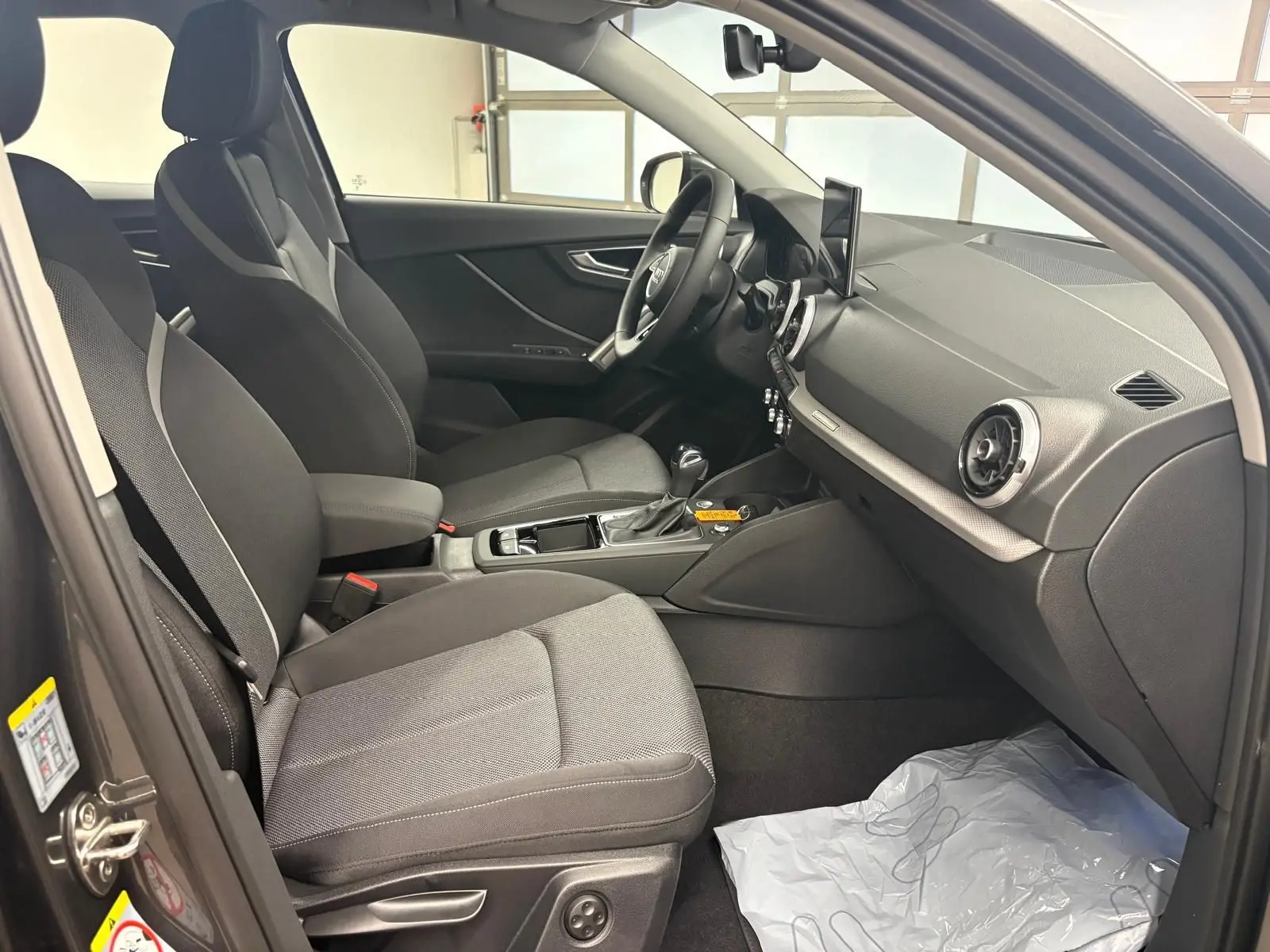 Vue intérieure côté conducteur de l'Audi Q2 35 TFSI S Line 2026 avec sièges tissu gris et tableau de bord moderne.