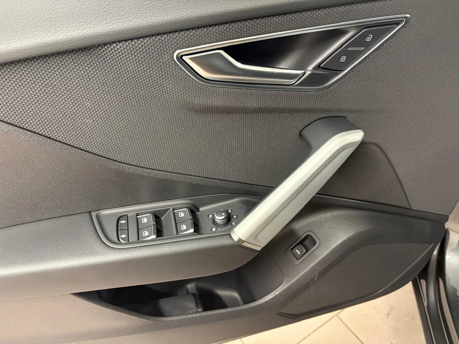 Gros plan sur la porte côté conducteur de l'Audi Q2 35 TFSI S Line 2026 en Gris Daytona, avec commandes de vitres et poignée argentée.