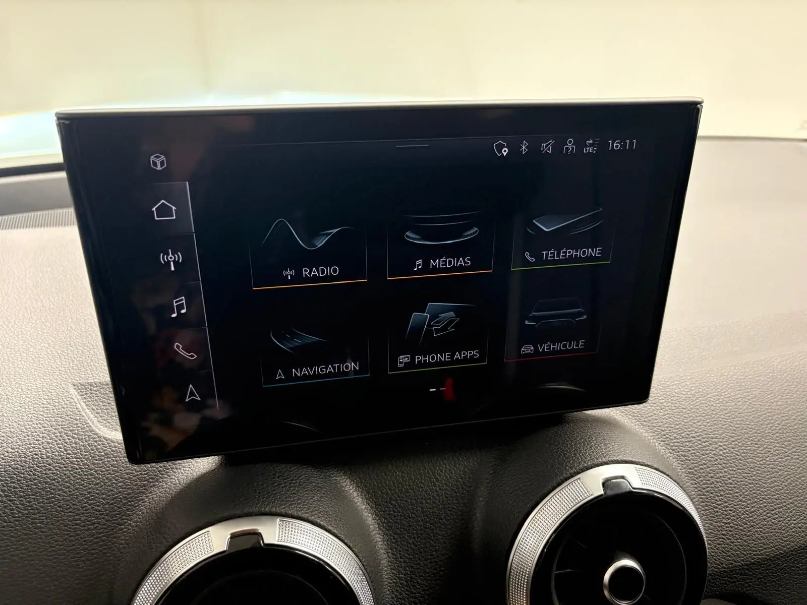 Écran tactile central de l’Audi Q2 35 TFSI S Line 2026, avec commandes multimédias et aérateurs ronds en dessous.