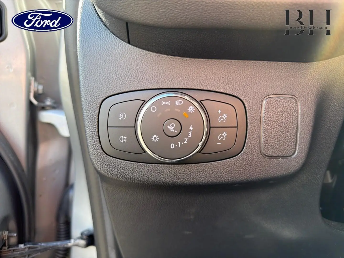 Gros plan sur le bouton de réglage des phares à gauche du tableau de bord du Ford Puma gris Solar Métallisée 2024.
