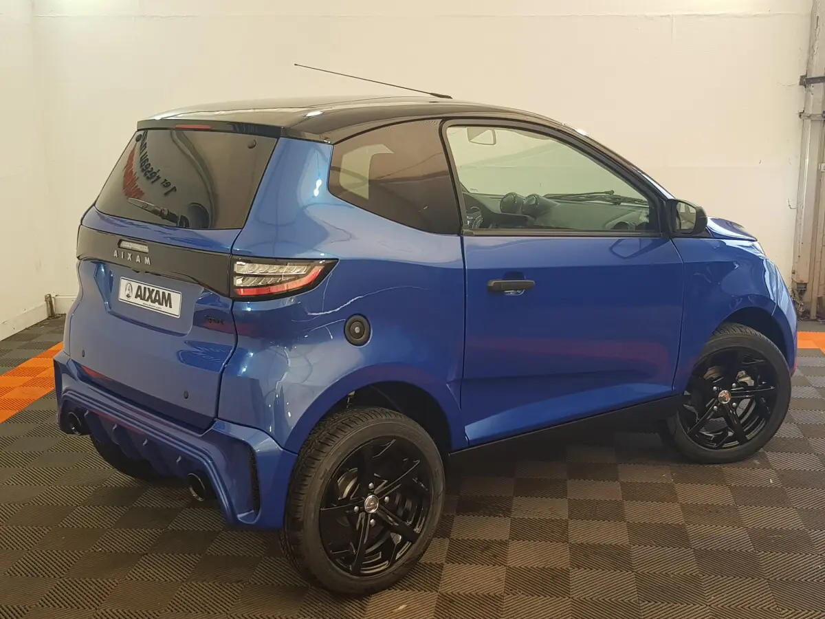 Vue 3/4 arrière droite d'une Aixam Ambition 0.5 City Sport bleu avec jantes noires et rétroviseur caméra côté gauche.