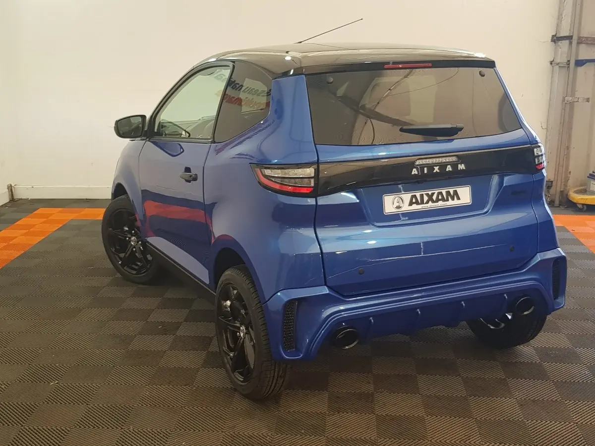 Vue 3/4 arrière d'une Aixam Ambition 0.5 City Sport bleu avec jantes noires et rétroviseur caméra côté gauche.