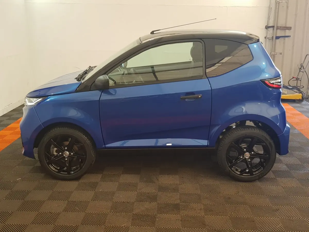 Vue de profil côté gauche d'une Aixam Ambition 0.5 City Sport bleu 2026 avec jantes noires et rétroviseur caméra.