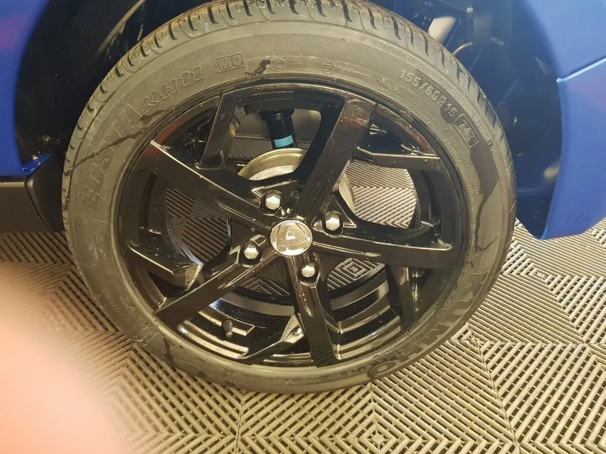 Gros plan sur la roue avant droite noire de l'AIXAM AMBITION 0.5 CITY SPORT bleu, mettant en valeur la jante sportive brillante.