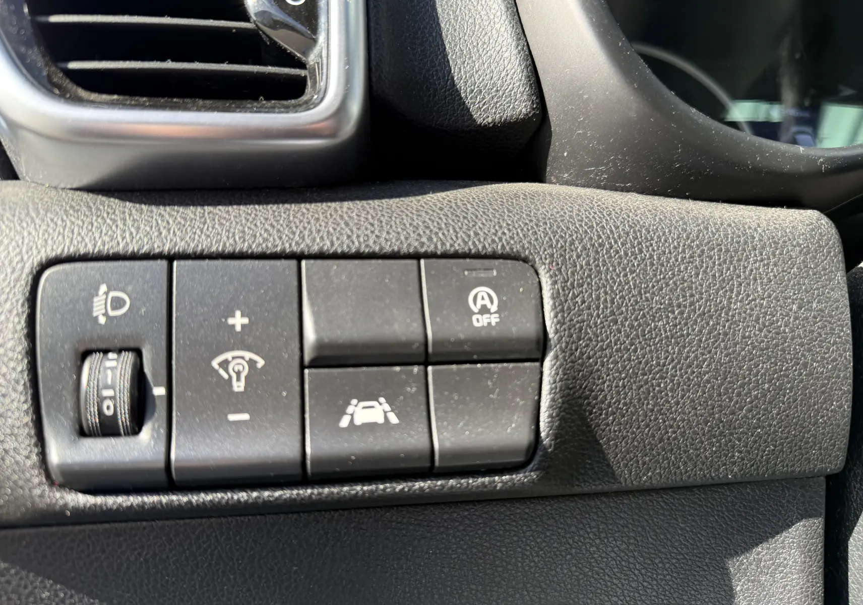 Gros plan sur les commandes de réglage d'éclairage et d'aides à la conduite à gauche du volant du Kia Sportage bleu 2021.