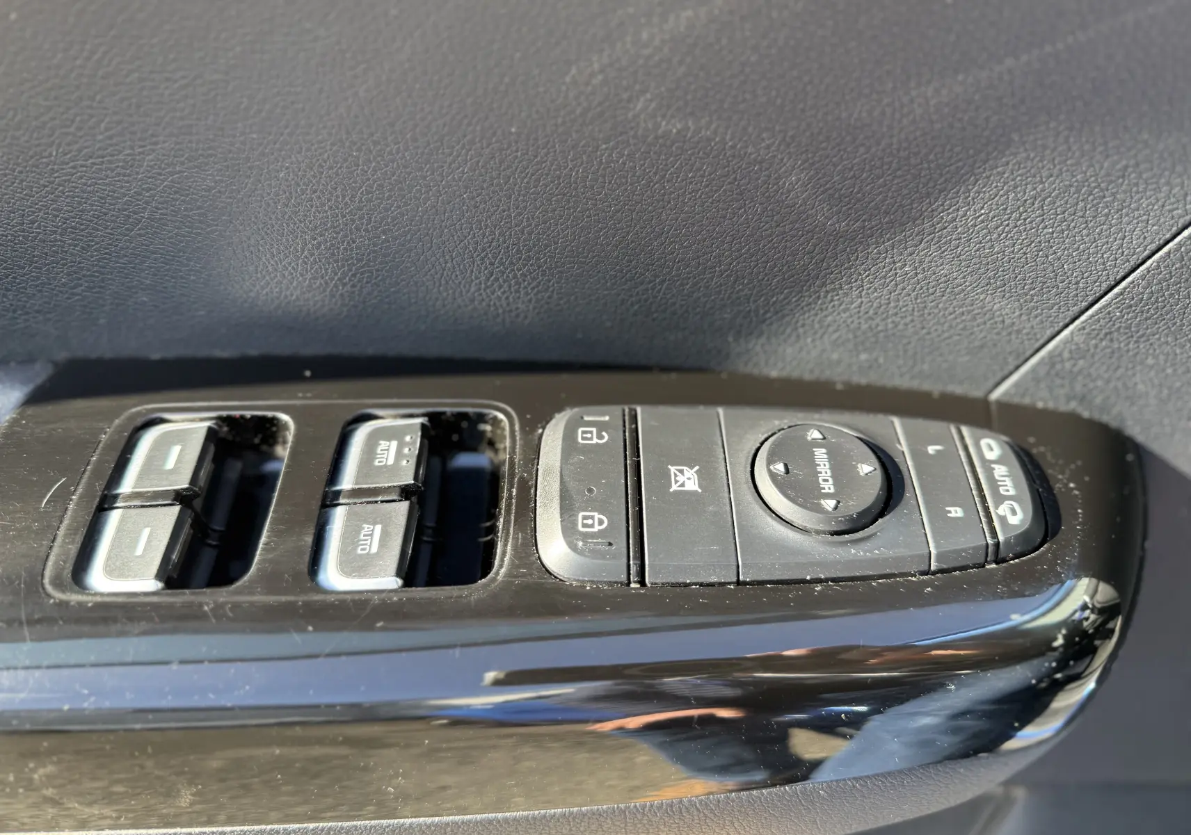 Gros plan sur les commandes de lève-vitres et rétroviseurs côté conducteur du KIA Sportage bleu 2021, finition Black Edition.