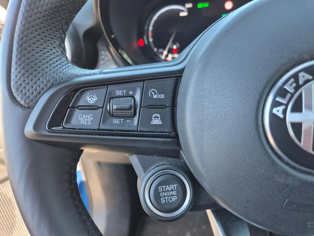Gros plan sur le volant sport noir de l'Alfa Romeo Tonale bleu, avec commandes de régulateur et bouton start/stop visibles.
