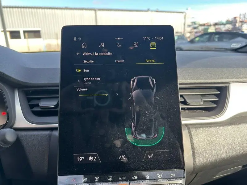 Écran tactile central du Renault Captur 2025 montrant l'aide au parking, tableau de bord et aérateurs en arrière-plan.