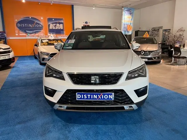Vue frontale d'un SEAT Ateca blanc Nevada exposé en showroom avec plaque Distinxion visible.