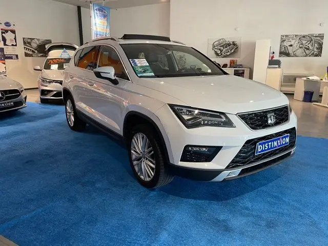 Vue 3/4 avant droite d'un SEAT Ateca blanc Nevada exposé en showroom avec plaques Distinxion visibles.