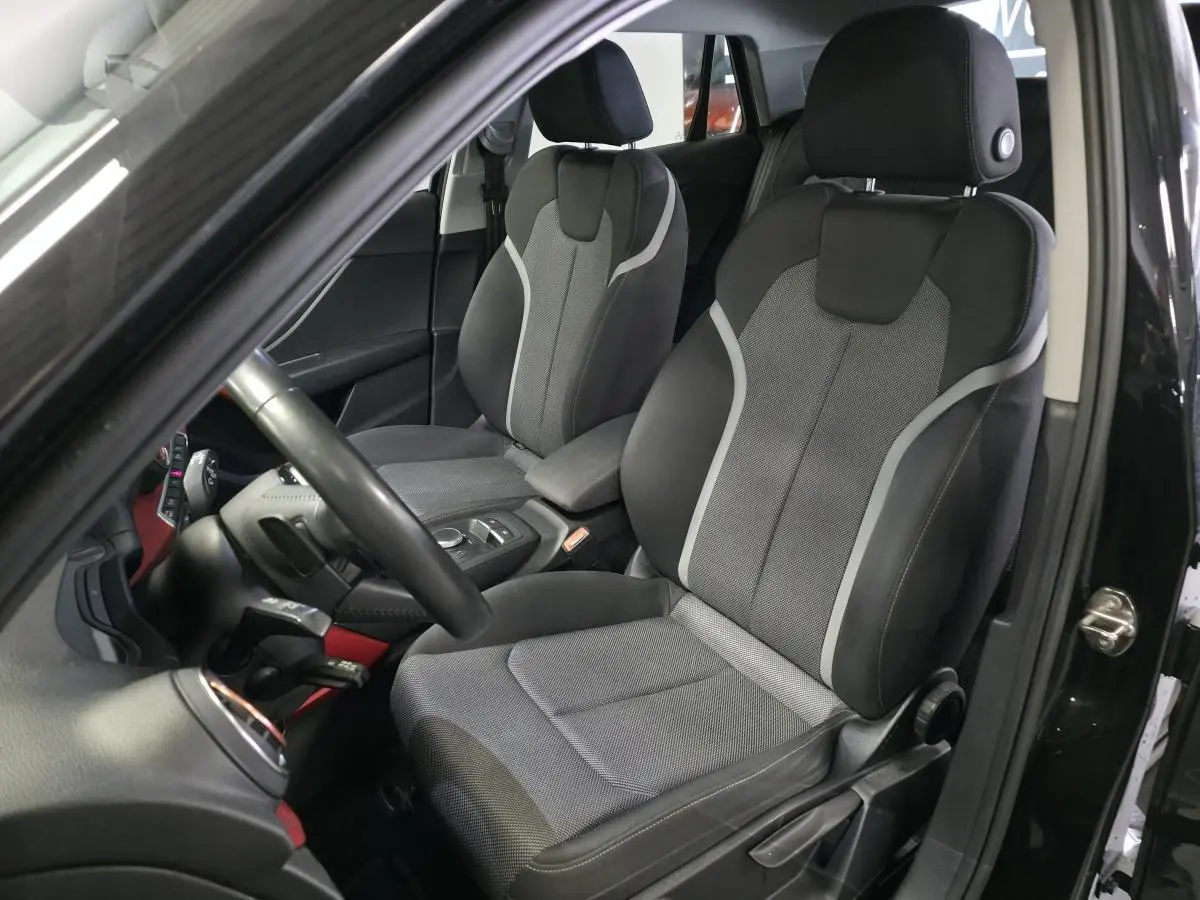 Vue intérieure côté conducteur de l'Audi Q2 noir avec sièges sport en tissu gris et applications décoratives rouges.