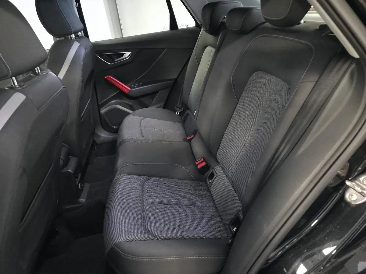 Vue intérieure arrière droite de l'Audi Q2 1.4 TFSI Sport 2017 avec sellerie noire et applications décoratives rouges.